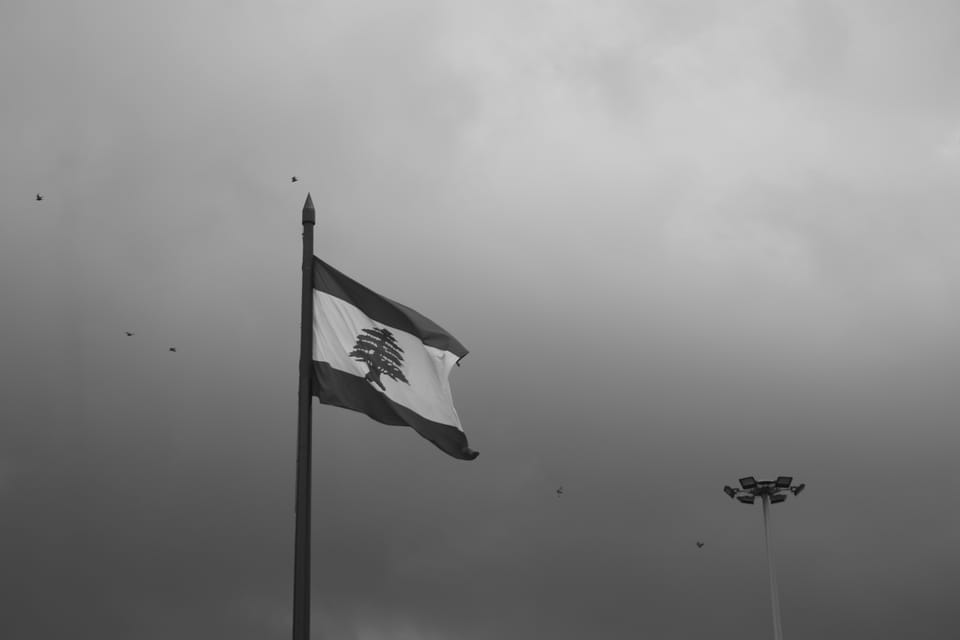 Black-and-white photograph of the Lebanese flag on a tall pole beneath a heavy overcast sky