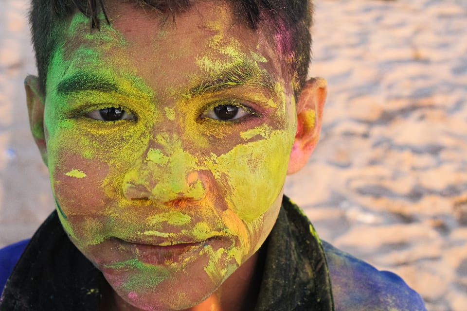 Close-up of a boy looking into the lens, his face covered in yellow and green festival powder