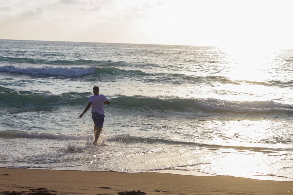 A man in a white t-shirt runs into the sea at golden hour as waves break in the sunlight