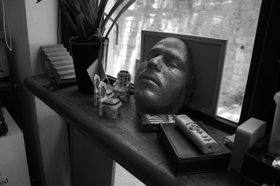 Black-and-white still life of a plaster face mask, miniature chairs and a remote on a windowsill